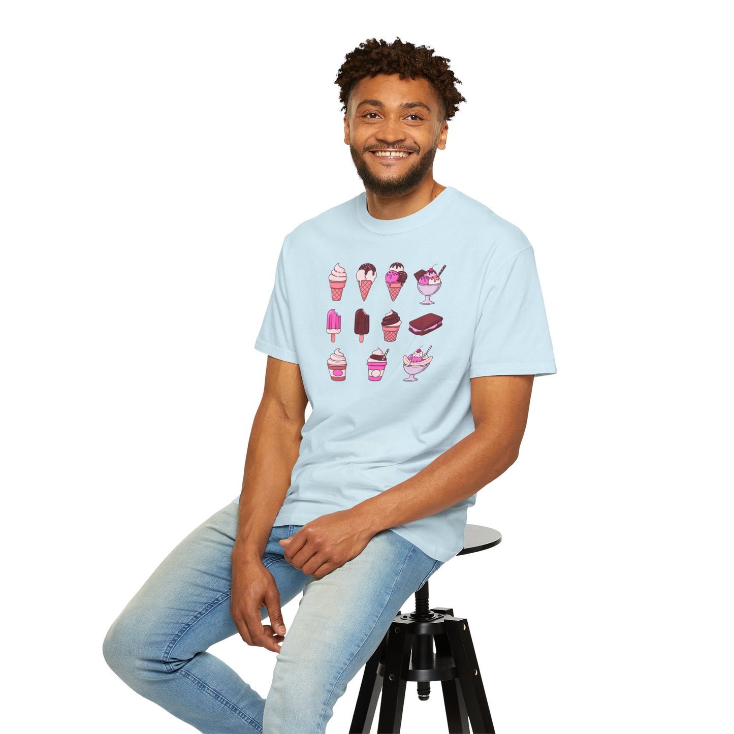 Man wearing a light blue t-shirt with ice cream graphics sitting on a stool against a white background